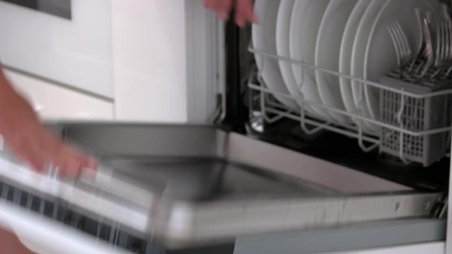 Housewife taking out clean plates from dishwasher machine. Female hands unloading dishwasher close up. Modern appliance at home.