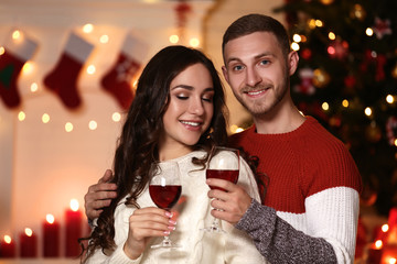 Happy young couple with wine in glasses sitting at home near christmas tree