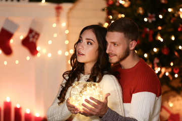 Obraz na płótnie Canvas Happy young couple holding glass bowl with garland near christmas tree