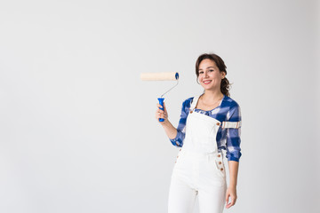 Repair, renovation, new home and people concept - young woman doing redecoration and show us thumbs up over white wall with copy space