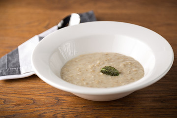 Oatmeal porridge on white plate with spoon on wooden background