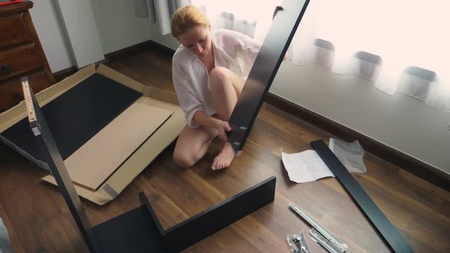 Assembling furniture at home, a housewife assembles a computer desk using hand tools.