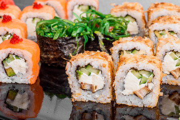 Maki Sushi set on dark pattern background. Sushi Set nigiri, rolls and sashimi served in black square plate