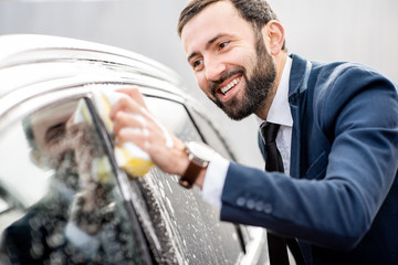 Elegant businessman dressed in the suit washing his car with yellow sponge on a self service open air car wash