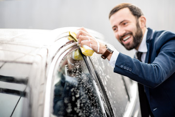 Elegant businessman dressed in the suit washing his car with yellow sponge on a self service open...
