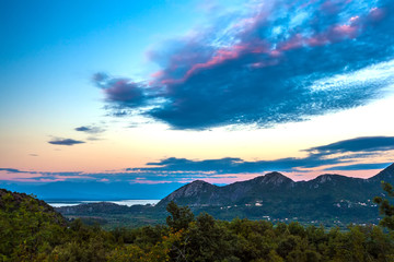 View of the coastal valley of the lake at dusk in the evening with poor lighting, beautiful green mountains under large blue clouds in the sky. Skadar Lake, Podgorica region, Montenegro.