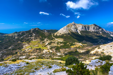 The top of the Lovcen mountain with a mobile communications tower installed, the rocky slopes are covered with green grass and trees and the road around. Vidikovac, Lovcen National Park, Montenegro.