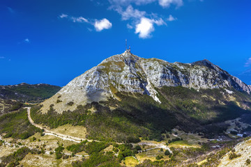 The top of the Lovcen mountain with a mobile communications tower installed, the rocky slopes are covered with green grass and trees and the road around. Vidikovac, Lovcen National Park, Montenegro.
