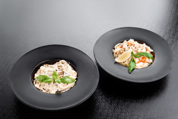 Tagliatelle pasta with mushrooms and cream cheese and tagliatelle pasta with seafood, decorated with basil in black plates isolated on a dark background. close up. top view