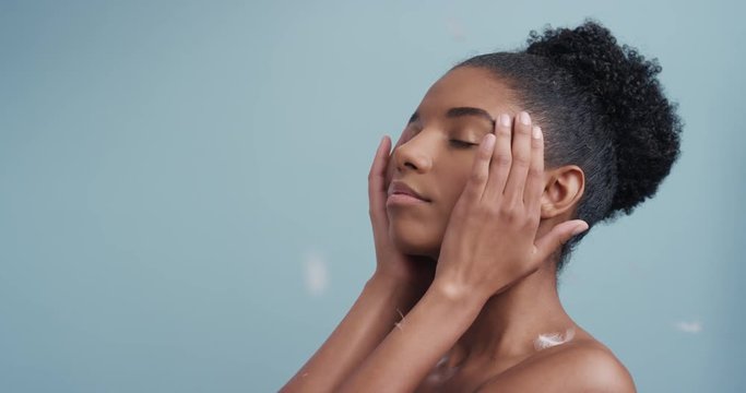 slow motion beauty portrait attractive african american woman feathers falling on smooth skin touching bare shoulders enjoying natural skincare gently caressing body in blue background  