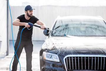 Professional washer in black uniform washing luxury car with water gun on an open air car wash