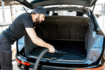Professional cleaner in black t-shirt and cap vacuuming trunk of a luxury big car outdoors