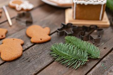 Fir branches in the foreground . A lot of ginger biscuits in different form on brown wooden table. Decorated with white sweet glaze. Christmas mood, winter morning.