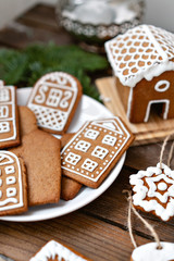 A lot of ginger biscuits in the form of European houses on a white plate. Decorated with white sweet glaze. Christmas mood, winter morning.