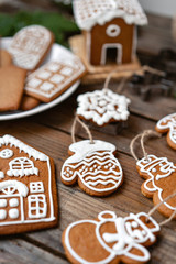 A lot of ginger biscuits in different form on brown wooden table. Decorated with white sweet glaze. Christmas mood, winter morning. Fir branches and forms for baking