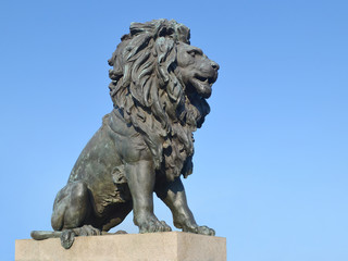Old statue of a lion on a stone pedestal against the blue sky close up