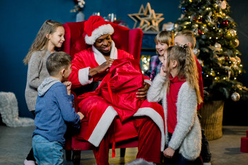 African Santa Claus takes gifts from a red bag for gifts and presents them to small, beautiful children.