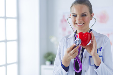A doctor with stethoscope examining red heart, isolated on white background