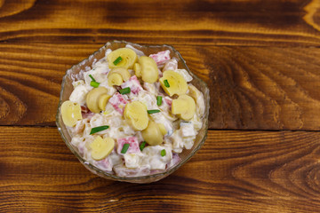 Potato salad with marinated mushrooms, sausage, onion and mayonnaise on wooden table