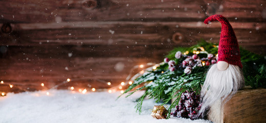 Weihnachtswichtel sitzt auf einem Holzbrett in winterlichter Dekoration und wartet auf Weihnachten - Banner, Header, Headline - Format - 234370004