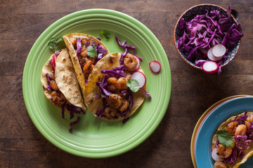 Several shrimp tacos on a green plate with a bowl of cabbage and onions