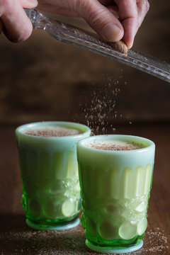 Person grating nutmeg as a garnish on a drink