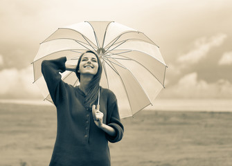 Beautiful adult girl in sweater with umbrella at wheat field and cloudscape on background. Image in...