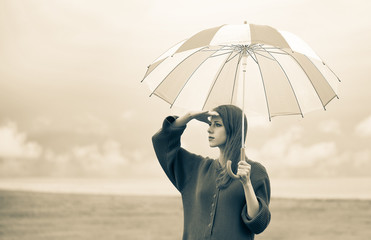 Beautiful adult girl in sweater with umbrella at wheat field and cloudscape on background. Image in...