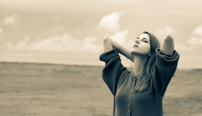 Beautiful adult girl in sweater at wheat field and cloudscape on background. Image in sepia color...