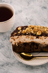Piece of cake on the plate. Metal dessert spoon. Tea in white mug. Light background.
