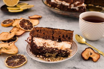 A portion of chocolate dessert. Brown dough and white meringue. Ground walnut. Dried slices of lemon and apples. Light background.