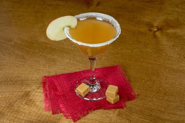 apple slice garnish on sugar rim martini cocktail glass with caramel candy and red burlap