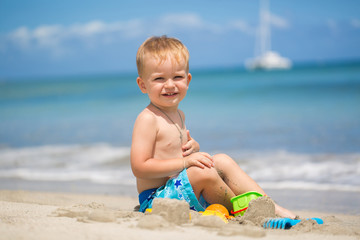 Cute baby boy playing with beach toys on tropical beach