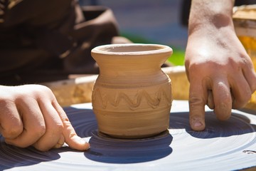 Fototapeta na wymiar Potter's hands separate a clay bowl from a pottery wheel with a thread, traditional art