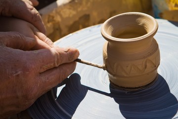 Fototapeta na wymiar Potter's hands make an ornament on clay bowl on a pottery wheel, girl learns to work with clay