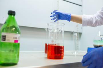 Hands of the scientist in the laboratory mixes with transfusion a chemical materials from graduated cylinder to beaker. Concept theme of applied chemistry - reaction, compound, solutions, dilution.