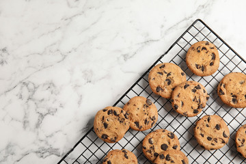 Cooling rack with chocolate chip cookies on marble background, top view. Space for text