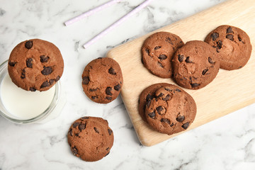 Wooden board with tasty chocolate chip cookies and milk on table, top view
