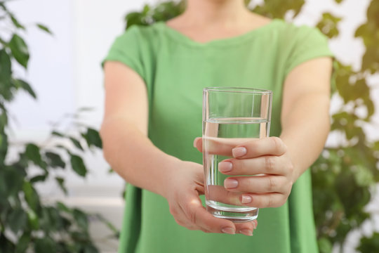 Woman holding glass of fresh water indoors, closeup