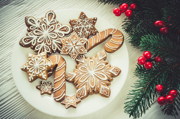 Christmas homemade gingerbread cookies and fir branches on white wooden background.