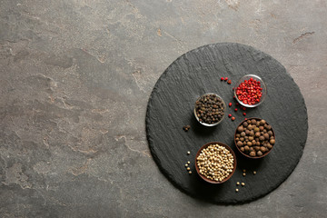 Slate plate with different types of pepper in bowls on gray background, top view. Space for text