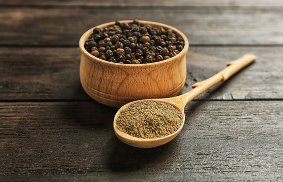Spoon with powdered black pepper and corns in bowl on wooden table