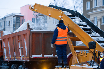 Obraz premium Snow cleaning tractor (snow-removal machine) loading pile of snow on a dump truck. Isolate. Snow plow outdoors cleaning street city after blizzard or snowfall