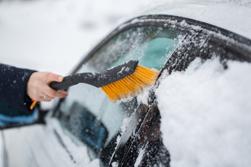 Woman cleaning snow from the car in the winter
