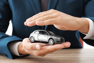 Insurance agent holding toy car over table, focus on hands - Powered by Adobe