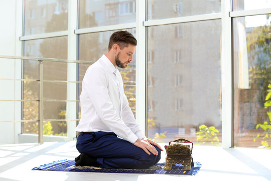 Muslim man with Koran praying on rug indoors