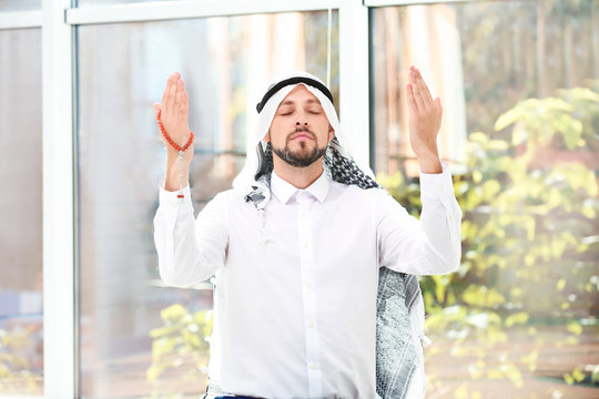 Muslim man with misbaha praying near windows indoors