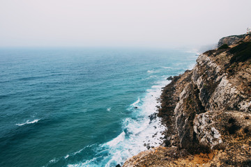 Fototapeta na wymiar Ocean coast line cliff in a cloudy fogy day..Aerial view of waves breaking to the rocky shore of Atlantic ocean in Portugal.