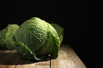 Fototapeta premium Savoy cabbage on wooden table against black background. Space for text