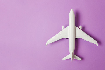 Simply flat lay design miniature toy model plane on violet purple pastel colorful paper trendy background. Travel by plane vacation summer weekend sea adventure trip journey ticket tour concept